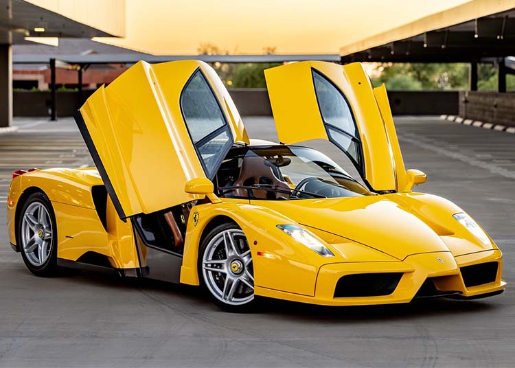A Ferrari Enzo in striking Giallo Modena with its butterfly doors open, parked in an empty rooftop parking lot.