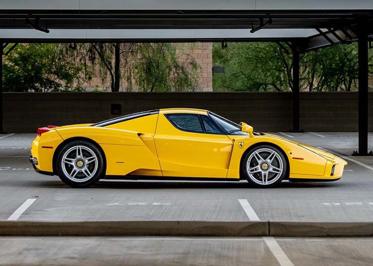 A Giallo Modena Ferrari Enzo sports car, featuring luxurious Cuoio Leather interior, parked in an empty, covered parking lot and viewed from the side.
