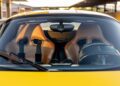 Interior view through the windshield of a Ferrari Enzo in Giallo Modena, showcasing two tan Cuoio leather bucket seats with racing seatbelts.