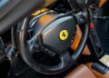 Close-up of a Ferrari steering wheel featuring the iconic Ferrari logo, various control buttons, and part of the luxurious Cuoio Leather interior—evoking the craftsmanship found in the legendary Ferrari Enzo.