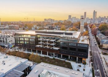 Aerial view of Rivian’s modern, multi-story Atlanta Headquarters with large windows and rooftop terraces, set in an urban neighborhood at sunrise with the city skyline in the background.