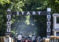 A Ferrari Formula 1 car approaches the starting line under a "START" banner at the Goodwood F80 Hillclimb, with people standing in the background along a tree-lined race track.