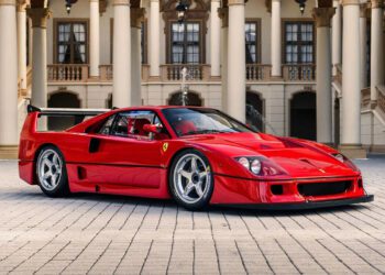 A red Ferrari F40 LM is parked on a cobblestone driveway in front of an ornate building with columns and arches, reminiscent of the elegance seen at RM Sotheby's Monterey Auction.