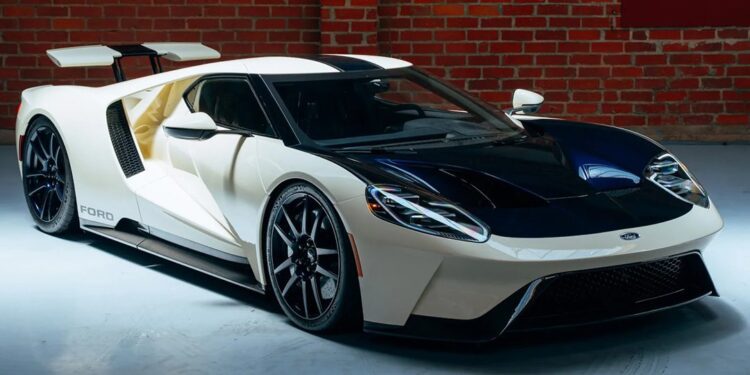 A white Ford GT sports car with black accents, an icon among exotic cars, is parked indoors on a light floor in front of a brick wall.