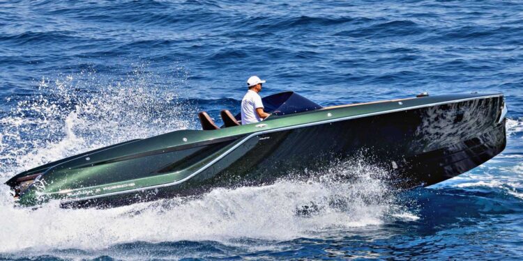 A person wearing a white cap pilots a sleek, modern Frauscher Fantom 850 speedboat at high speed across blue ocean water, creating a large spray.
