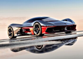 A sleek, futuristic red and black sports car with aerodynamic design is parked on a reflective surface under a clear sky—reminiscent of the California Corvette: GM's Pasadena Studio showcases this stunning one-off hypercar concept.