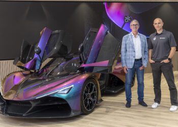 Two men stand next to a Zenvo sports car with open butterfly doors in a modern showroom, ready for Goodwood.