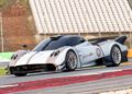 A white and gray Pagani sports car with the number 1 on the door drives on a racetrack during hillclimb runs, with empty bleachers in the background.