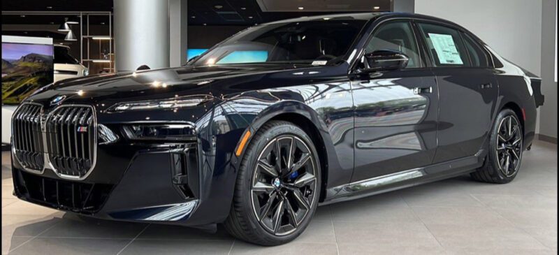 A black BMW sedan is displayed in a showroom with a price sticker visible on the rear window, showcasing some of the best lease deals for those seeking a new car lease.