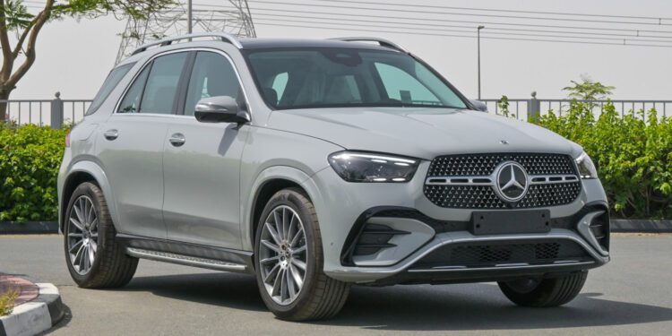 A silver Mercedes-Benz SUV parked near greenery and a metal fence, with power lines in the background—showcasing a top choice for those seeking the best car lease deals.