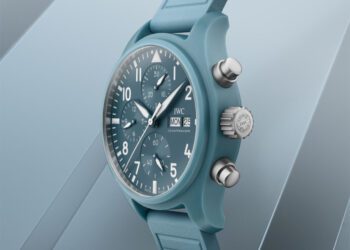 A blue IWC Miramar Pilot’s Chronograph wristwatch with a blue rubber strap, showing the time 10:08, date 25, and day Monday, set against a matching blue geometric background.