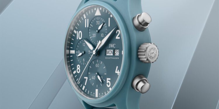 A blue IWC Miramar Pilot’s Chronograph wristwatch with a blue rubber strap, showing the time 10:08, date 25, and day Monday, set against a matching blue geometric background.