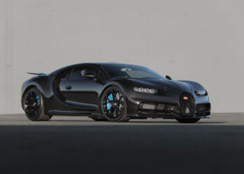 A black Bugatti Chiron sports car sits parked on a paved surface in front of a plain gray wall, soon to be showcased by Broad Arrow at the 2025 Monterey Auction.