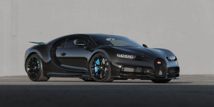 A black Bugatti Chiron sports car sits parked on a paved surface in front of a plain gray wall, soon to be showcased by Broad Arrow at the 2025 Monterey Auction.