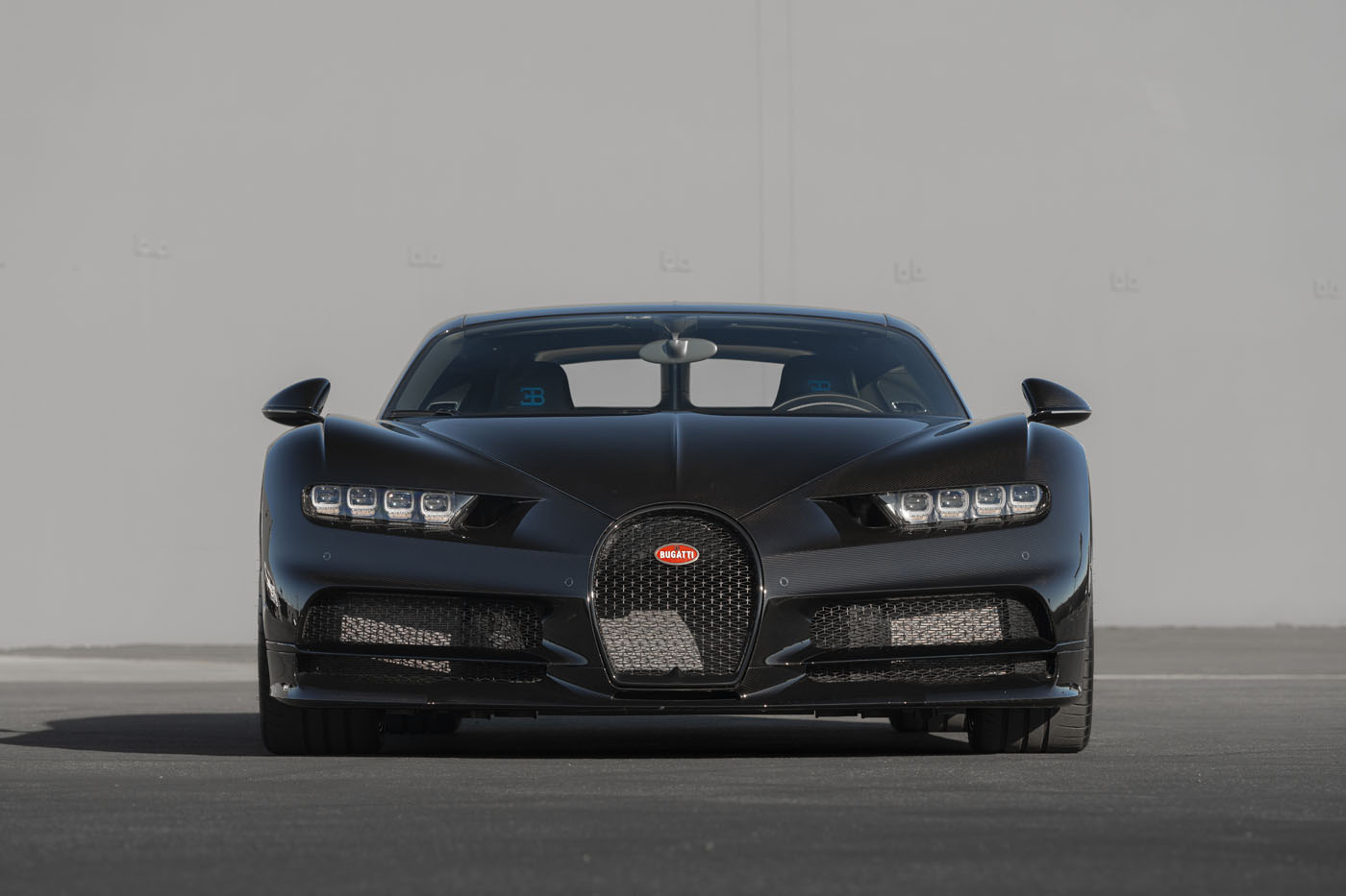 Front view of a black Bugatti Chiron parked on clean asphalt, set against a plain gray wall—a striking image from the Monterey Jet Center Auction presented by Broad Arrow.
