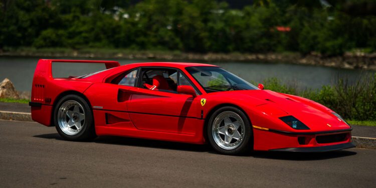 A 1991 Ferrari F40 sports car is parked on a paved road with greenery and a body of water in the background, reminiscent of those showcased at the Monterey Jet Center Auction.