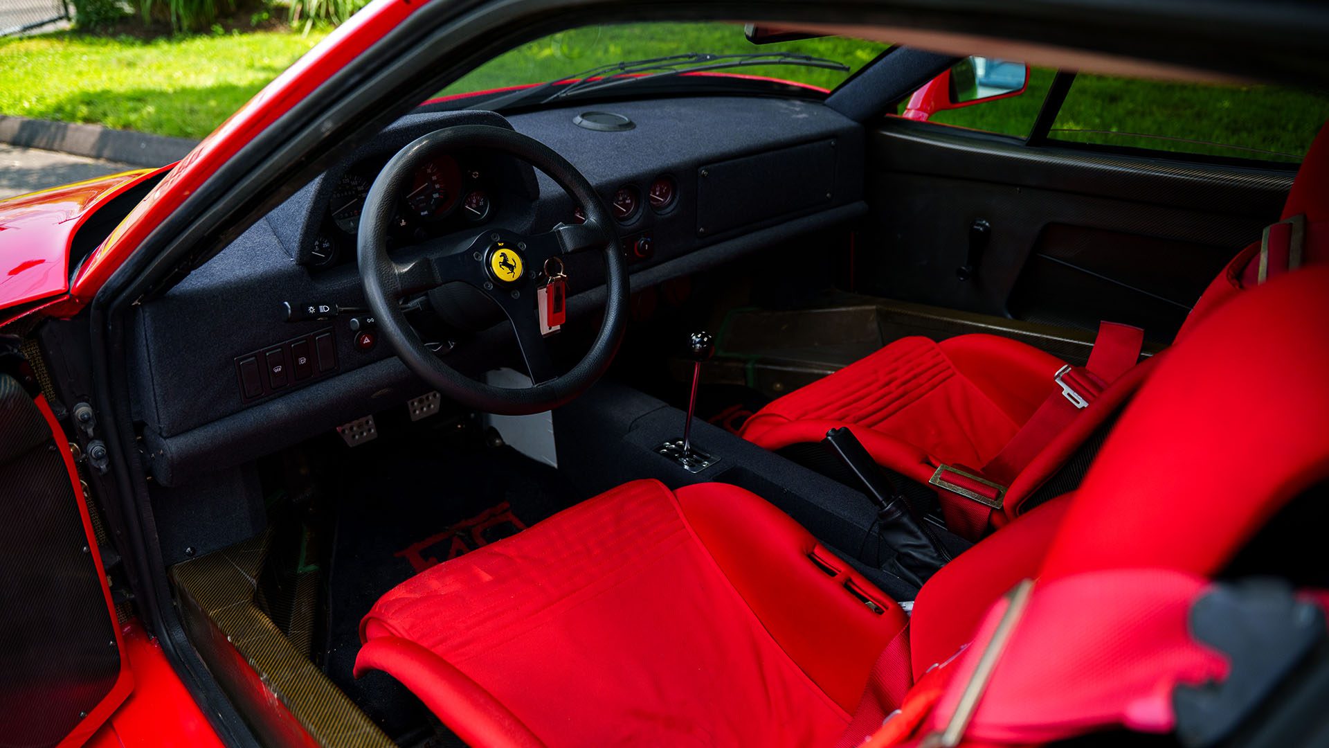 Interior of a Ferrari F40 sports car with striking red bucket seats, a black steering wheel featuring the Ferrari logo, and a minimalist dashboard—set to be showcased by Broad Arrow at the 2025 Monterey Auction.