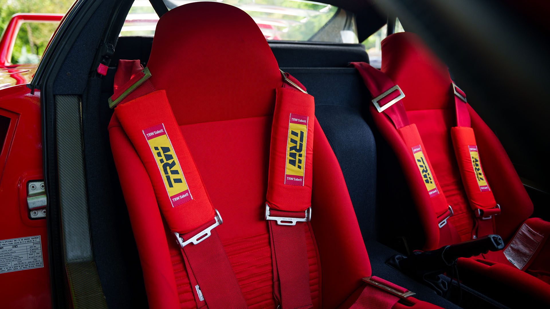 Close-up of two red racing bucket seats with TRD-branded four-point harnesses inside a 1991 Ferrari, captured at the Monterey Jet Center Auction.
