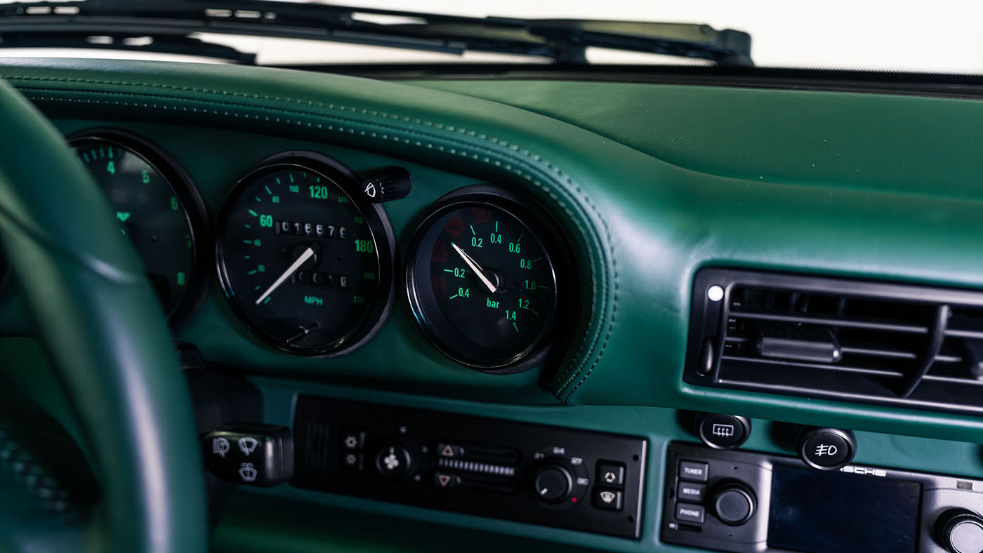 Close-up of a classic car dashboard, featuring speedometer, tachometer, air vent, and control buttons with green interior finish—captured at the 2025 Monterey Jet Center Auction by Broad Arrow with the RUF CTR 2 Sport on display.