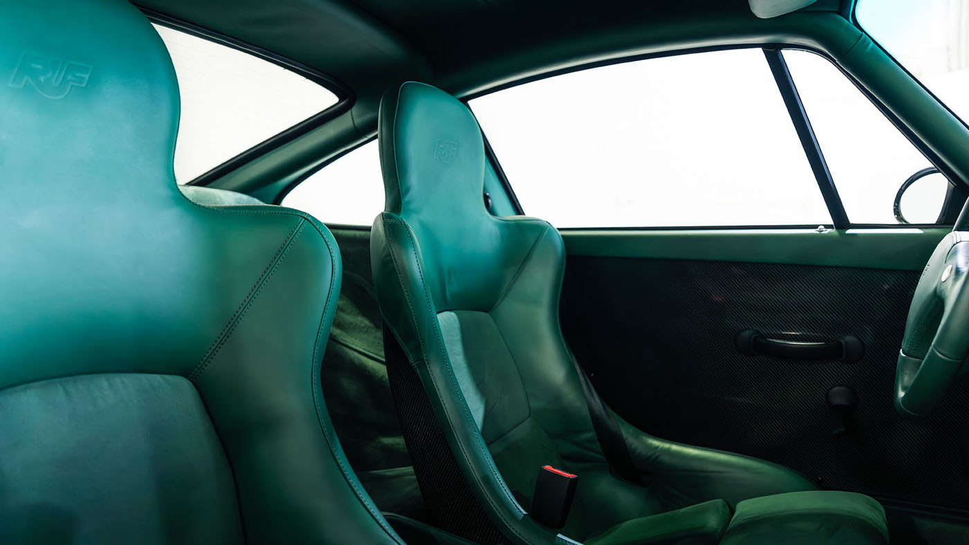 Interior view of a classic RUF CTR 2 Sport with two green leather bucket seats, a manual window crank, and a sunlit window—an icon showcased at the 1998 Monterey Jet Center Auction.