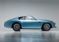 Side view of a vintage blue DB4 GT Zagato Continuation with sleek curves, chrome wire wheels, and a minimalist background.