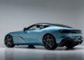 A sleek, blue Aston Martin DBS GT Zagato with a black roof is parked in a studio with a plain gray background, shown from a rear side angle.