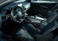 Interior of a luxury sports car, inspired by the Aston Martin DBS GT Zagato, featuring black leather seats, a digital display, and a modern dashboard with metallic and carbon fiber accents.