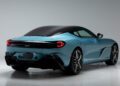 A blue Aston Martin DBS GT Zagato with a black roof is viewed from the rear left angle, featuring sleek lines, large wheels, and distinctive tail lights, set in a studio with a plain background—perfect for the Monterey Jet Center Auction.