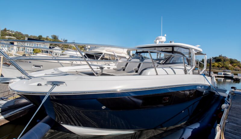 White and blue motorboat docked at a marina, surrounded by luxury yachts and waterfront houses in the background under a clear blue sky, capturing an unforgettable maritime experience.