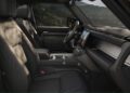 Front interior view of the redesigned Defender SUV showing black leather seats, a central touchscreen display, and mountain scenery visible through the windows—highlighting its latest design updates.