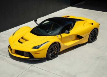 A yellow Ferrari LaFerrari hypercar is parked on a smooth, light-colored concrete surface near a dark wall.