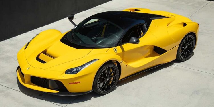A yellow Ferrari LaFerrari hypercar is parked on a smooth, light-colored concrete surface near a dark wall.