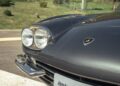 Close-up of the front left side of a vintage Lamborghini car, showing dual headlights, part of the bumper, and the iconic badge—a timeless icon from Emilia-Romagna perfect for driving enthusiasts.