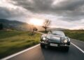 A Vintage Lamborghini cruises along a winding rural road at sunset in Emilia-Romagna, framed by lush green hills and dramatic clouds.