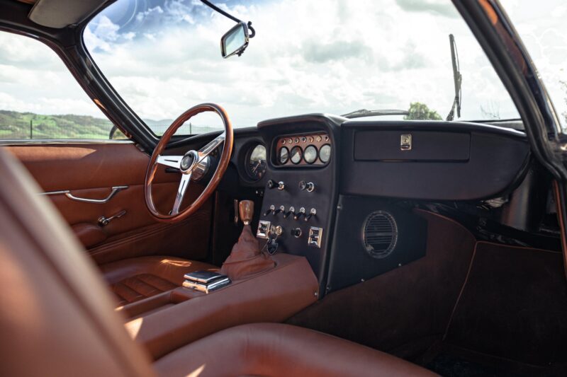 Classic car interior with brown leather seats, a wooden steering wheel, analog gauges, and manual gear shift; reminiscent of Vintage Lamborghinis cruising through the countryside of Emilia-Romagna.