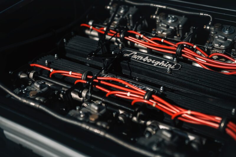 Close-up view of a Lamborghini engine with red ignition wires and metallic components, capturing the spirit of driving Vintage Lamborghinis through the heart of Emilia-Romagna.