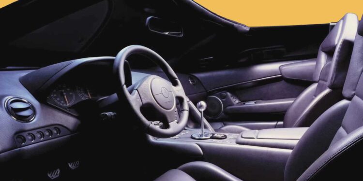 Interior view of an open-top Lambo sports car with black leather seats, a manual gear shift, and a steering wheel, with a yellow background visible through the windows.