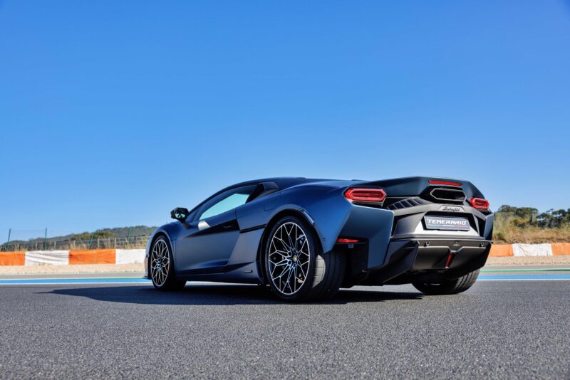 A matte black Lamborghini Temerario is parked on a race track under a clear blue sky, viewed from the rear left angle—perfect for a thrilling track review.