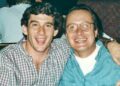 Two men are sitting close together, smiling at the camera. One wears a plaid shirt, and the other—wearing glasses and a blue shirt—sports a McLaren logo, hinting at their shared enthusiasm for the legendary Road Car Collection of Mansour Ojjeh.