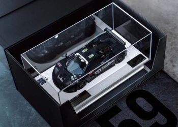 A black McLaren F1 GTR model race car with the number 59 is displayed in a glass case with a white base, inside a black Lanzante box featuring the number 59, celebrating its iconic Goodwood legacy.