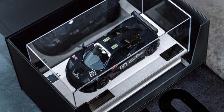 A black McLaren F1 GTR model race car with the number 59 is displayed in a glass case with a white base, inside a black Lanzante box featuring the number 59, celebrating its iconic Goodwood legacy.