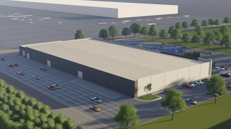A large industrial warehouse with a parking lot, surrounded by trees and cars, seen from an elevated angle in daylight, marks the spot where McLaren Doubles Down on America with its new $10.5m Vehicle Processing Center in Baltimore.