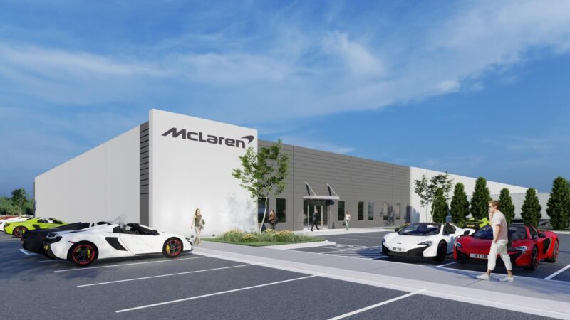 A modern McLaren building with large signage, several sports cars parked in front, and people walking near the entrance on a sunny day as McLaren doubles down on America with its new $10.5m Vehicle Processing Center in Baltimore.