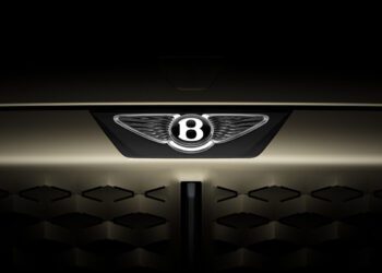 Close-up of the front grille of a car featuring the illuminated Bentley logo with a dark, shadowed background.