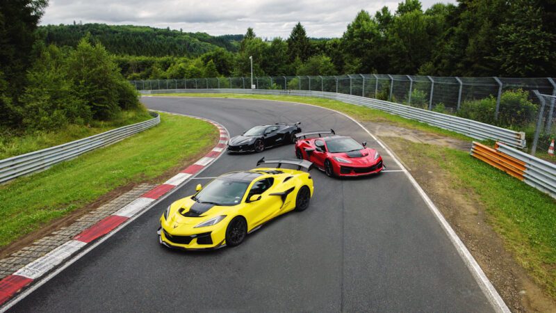 Three brightly colored sports cars—yellow, black, and red—are parked on a curve of a racetrack surrounded by greenery and safety barriers, including the legendary Corvette ZR1, one of the fastest American production cars to lap the Nürburgring.