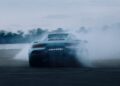 A 2026 Maserati MCPURA debuts at Goodwood, drifting on an empty road and producing a large cloud of tire smoke; trees and a cloudy sky are visible in the background as its liquid crystal roof glimmers.