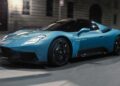 A blue 2026 Maserati MCPURA, debuting at Goodwood with an advanced liquid crystal roof and F1 tech, drives on a city street at night.