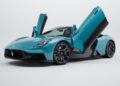 A blue 2026 Maserati MCPURA with butterfly doors open, featuring an F1 tech-inspired liquid crystal roof, viewed from the front left side against a plain white background.