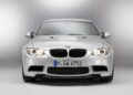 Front view of a silver BMW E90 M3 with headlights on, photographed in a studio with a plain background—an iconic collector car showcased in pristine condition.