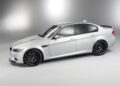 A silver BMW E90 M3 sedan, considered a true collector car, is parked in a studio with a plain, light gray background.